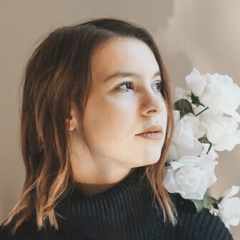 A beautiful woman in a dark navy turtleneck looks on heavenly, as white flowers sit on her left shoulder.