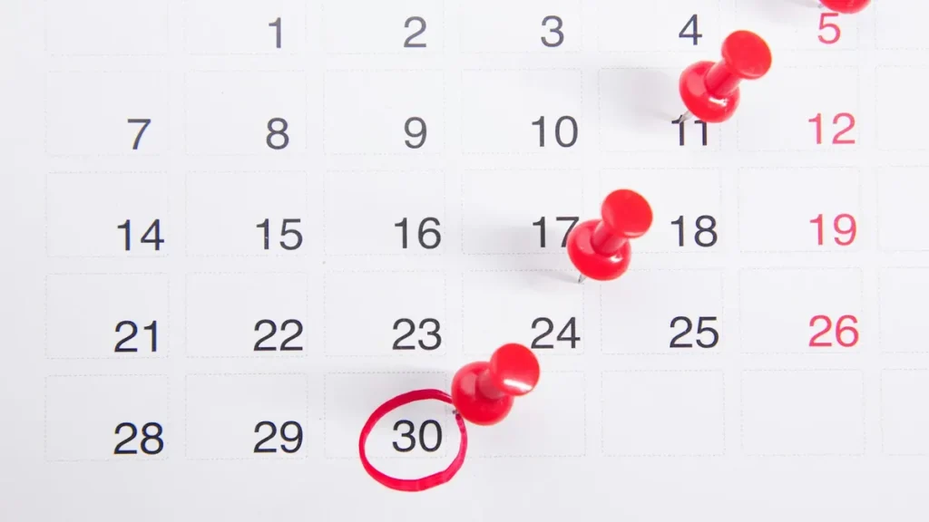 A wall calendar with red pins marking dates through the month, one date circled in red.